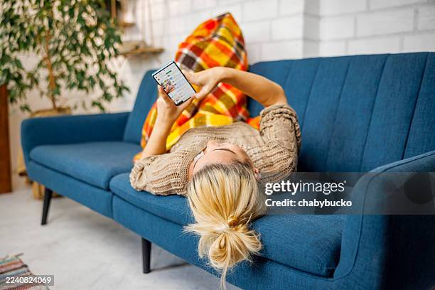 woman shopping online while lying on sofa at home - op de rug liggen stockfoto's en -beelden