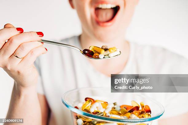 a close-up shot of a person's open mouth and a spoon filled with various pills and capsules, as if about to eat them. - durability stock pictures, royalty-free photos & images