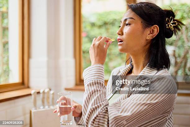 asian woman taking a health supplement or vitamin with glass of water - vitamin stock pictures, royalty-free photos & images