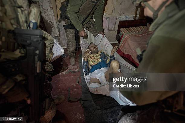 Ukrainian Marines help carry an injured elderly man with a broken leg to a volunteer's car for evacuation from the city on October 16, 2025 in...