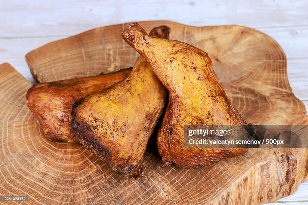 Close-up of three smoked chicken drumsticks on a rustic wooden cutting board, ready for a meal