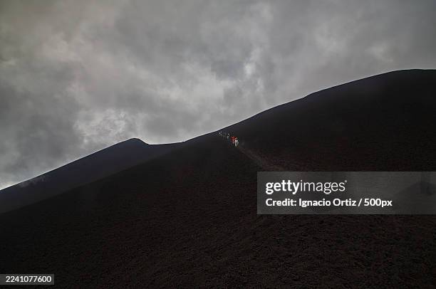 hikers ascend a steep volcanic ash dune under a dramatic cloudy sky, showcasing determination and the challenge of the natural landscape,zafferana etnea,italy - difficult path stock pictures, royalty-free photos & images