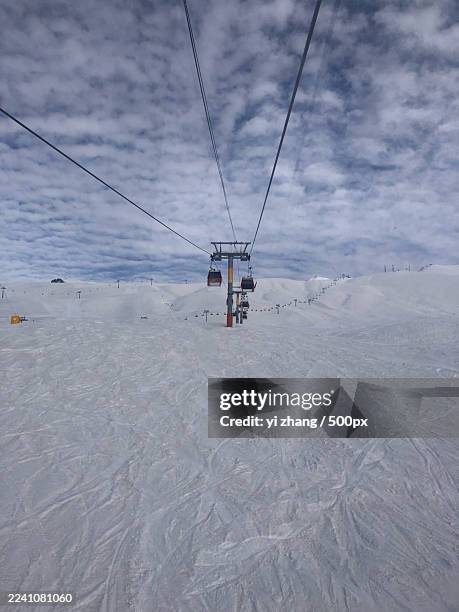 low angle view of an overhead cable car against a cloudy sky over a snowy mountain landscape - ski pole stock pictures, royalty-free photos & images