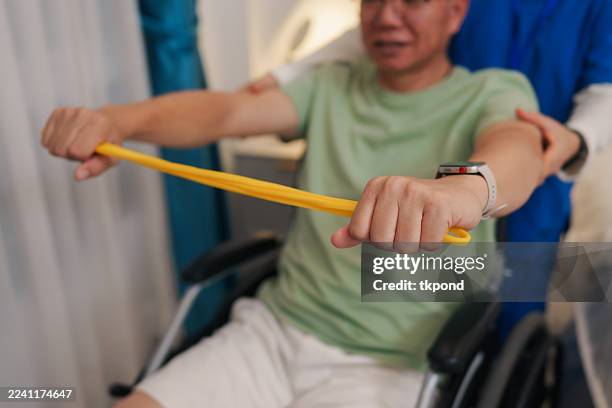 senior man in wheelchair doing arm exercises with resistance bands, assisted by a caregiver - neuropathy stock pictures, royalty-free photos & images
