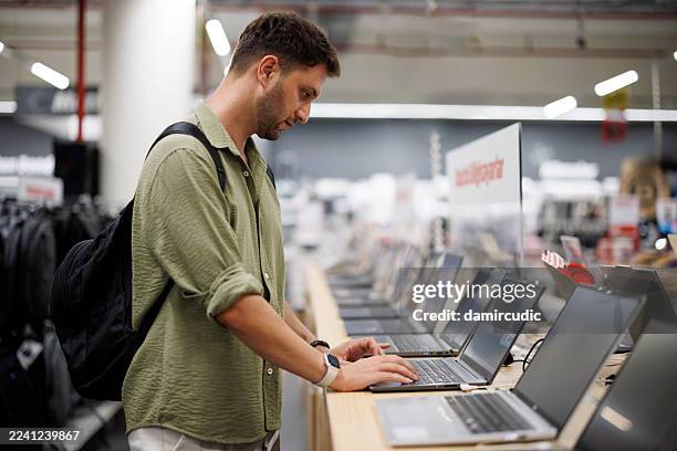 moderner männlicher kunde, der laptop im einzelhandel computergeschäft wählt - elektrogeschäft stock-fotos und bilder