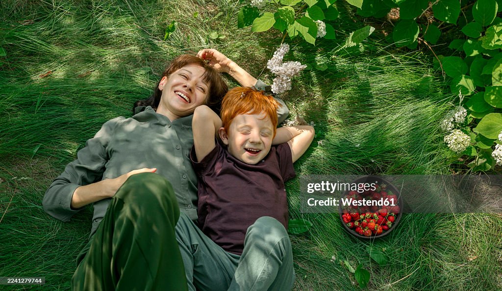 Mother and son with red hair laughing together on grass with berries
