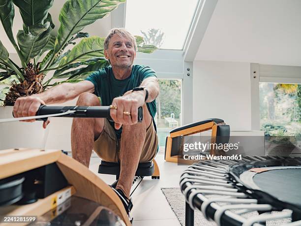 man exercising on rowing machine at home in modern living room - baby boomer stock-fotos und bilder