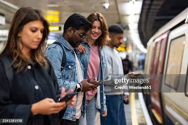 commuters using smartphones while waiting on london underground platform - packed commuter train stock pictures, royalty-free photos & images