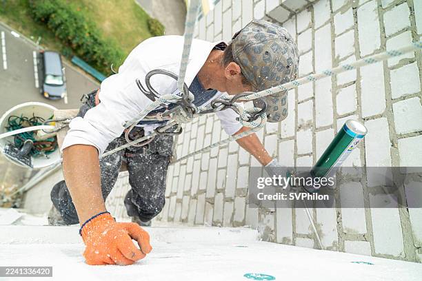 construction worker filling gaps between polystyrene panels with expanding foam during building facade insulation. - wall cladding stock pictures, royalty-free photos & images