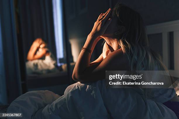 woman sitting up in bed at night with hands over face, reflecting in mirror - warm light stock pictures, royalty-free photos & images