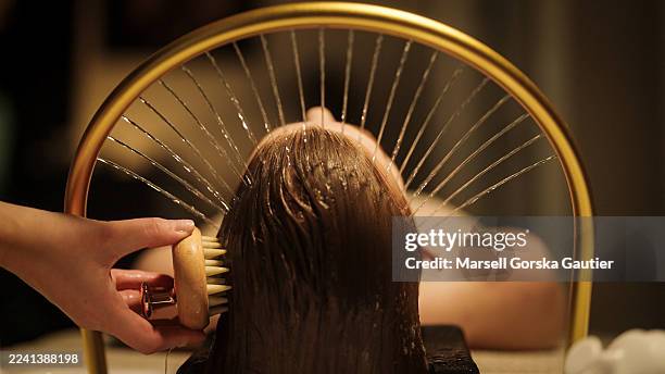 a woman lies under a water massager – aureola. a hand massages the head with a comb. shot from behind. - spa bildbanksfoton och bilder