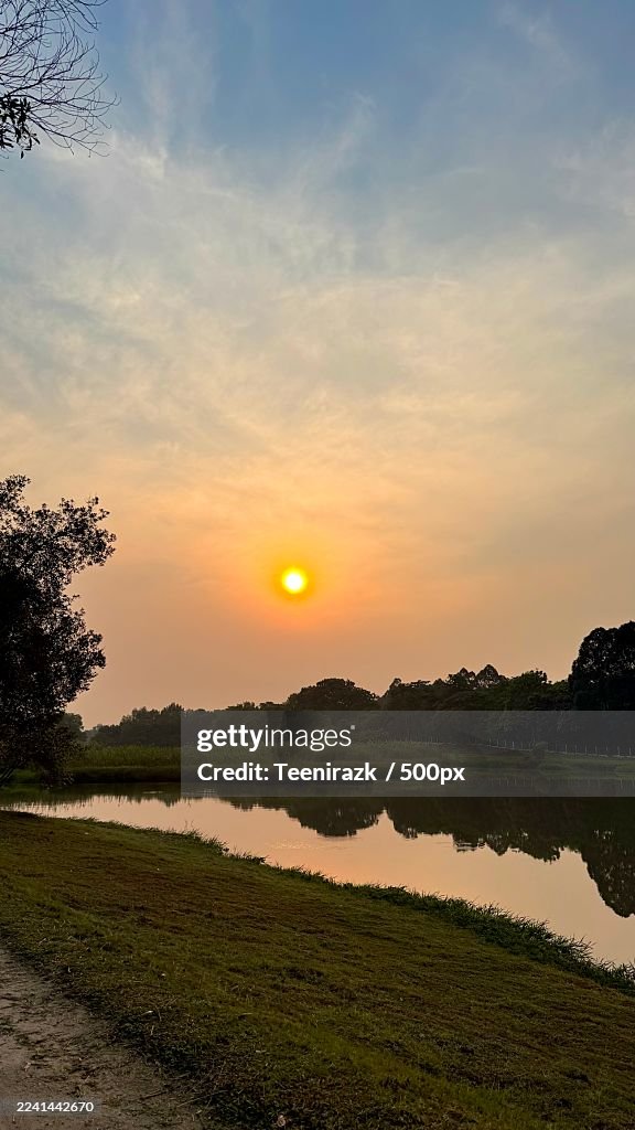 Scenic view of a tranquil lake reflecting the vibrant sunset sky with lush trees on the horizon