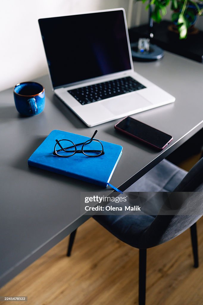Modern Home Office Desk With Laptop, Blue Notebook, Glasses, And Smartphone
