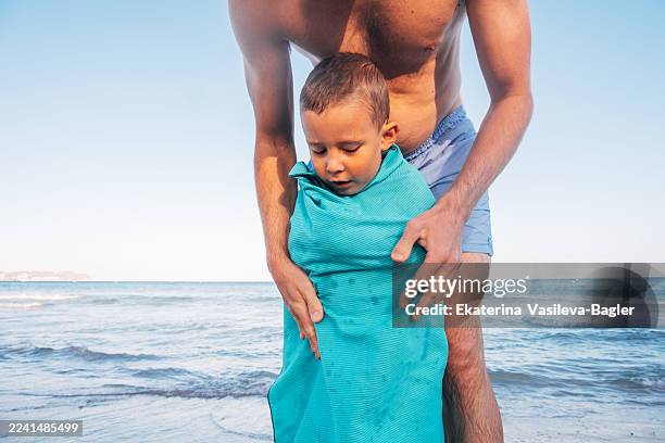 loving father wrapping young son in a warm towel after swimming in the sea - envuelto en una toalla fotografías e imágenes de stock