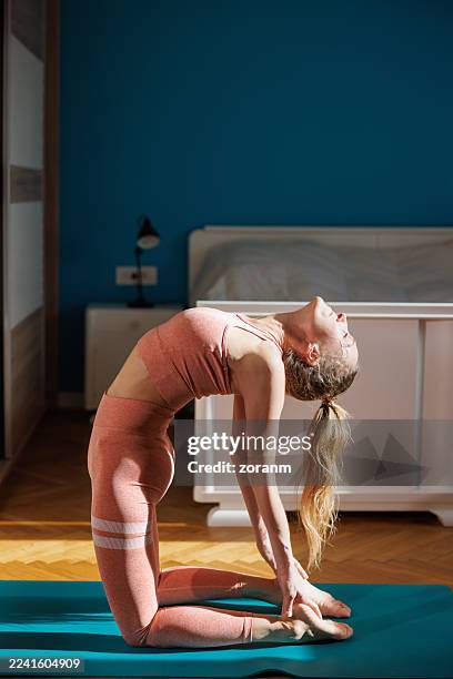 donna di mezza età che pratica yoga sul pavimento della camera da letto, inginocchiandosi e piegandosi all'indietro - piegarsi allindietro foto e immagini stock