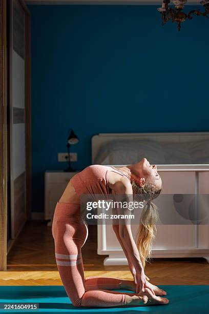 donna matura che pratica yoga sul pavimento della camera da letto, inginocchiandosi e piegandosi all'indietro - piegarsi allindietro foto e immagini stock