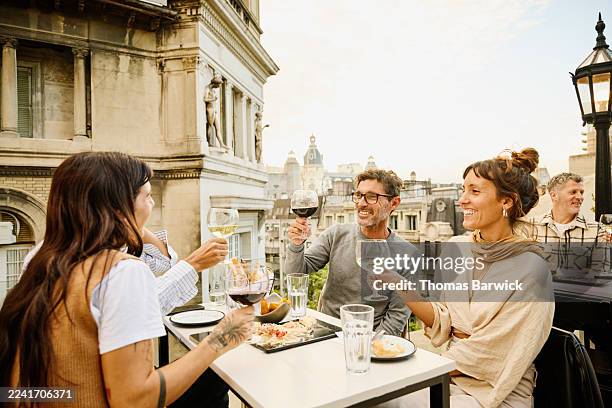 medium shot friends holding up wineglasses at rooftop restaurant - buenos aires stock pictures, royalty-free photos & images