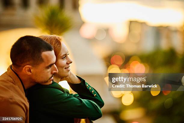 medium shot couple leaning on balcony looking at city view at night - weichzeichner stock-fotos und bilder