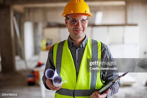 confident construction engineer holding blueprints and a clipboard - civil engineer stock pictures, royalty-free photos & images