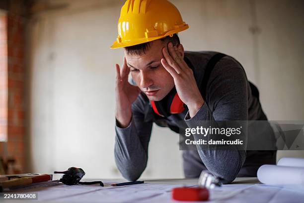 stressed construction worker reviewing blueprints at a construction site - construction mistake stock pictures, royalty-free photos & images