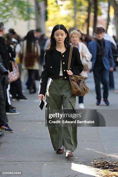 Guest wears long straight black hair with a center part, a brown leather shoulder bag with an adjustable strap and buckle, a black cropped textured...