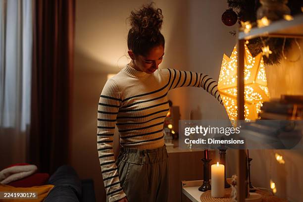 gemütlicher weihnachtsabend mit einer frau, die einen warmen, kerzenbeleuchteten raum mit festlicher beleuchtung dekoriert - kerzenleuchter stock-fotos und bilder