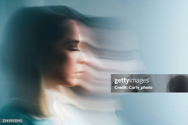 the woman's face is captured in profile with her eyes closed, her outline receding into a horizontally blurred, striped phantom image against a pale background. - despair stock pictures, royalty-free photos & images