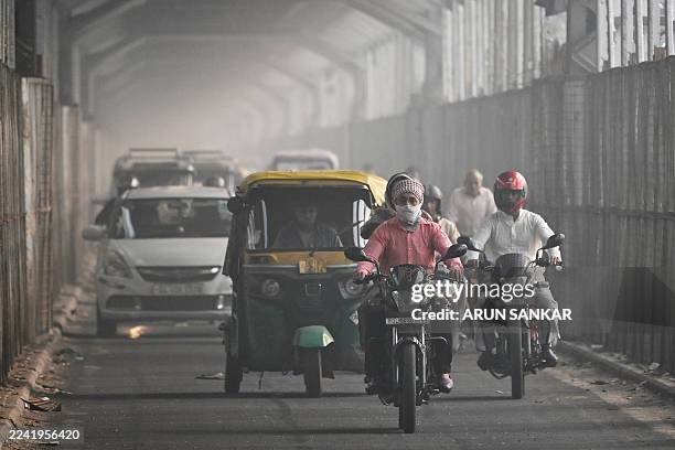 Commuter with his face covered in cloth rides along a bridge across river Yamuna in New Delhi on October 21 as smog engulfed the city skyline a day...