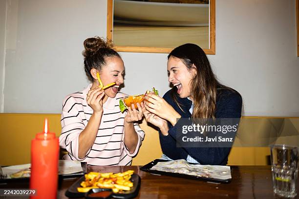 glückliche junge frauen, die eine mahlzeit teilen, fast food genießen und tiefe freundschaft schließen, während sie gemeinsam in einem diner spaß haben - sharing stock-fotos und bilder