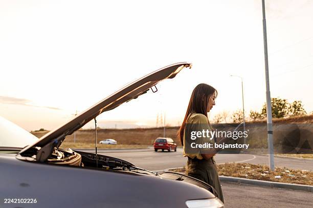 stressed asian woman using smart phone to call roadside assistance after car breakdown on quiet rural road - assistência na estrada imagens e fotografias de stock