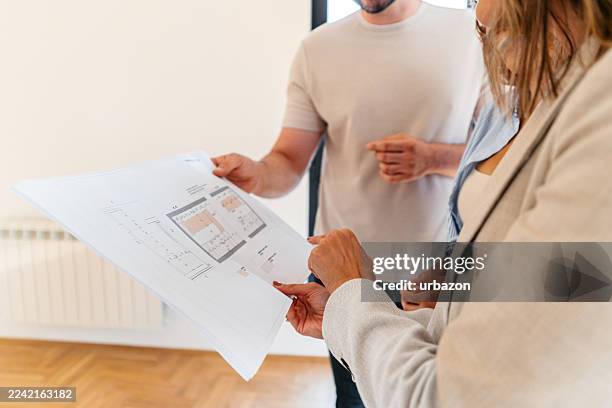 female architect showing the design blueprint to the young couple - real estate developer stock pictures, royalty-free photos & images