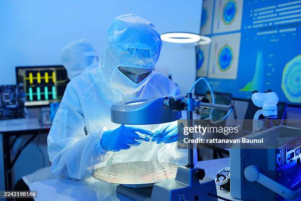 engineers in sterile suits work at a semiconductor manufacturing plant using microscopes in a lab. - clean suit stock pictures, royalty-free photos & images