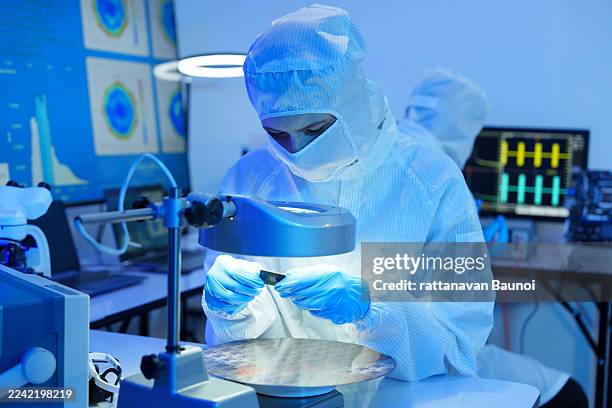 engineers in sterile suits work at a semiconductor manufacturing plant using microscopes in a lab. - nanotecnologia imagens e fotografias de stock