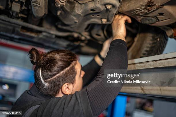 mechanic working under lifted car in auto repair shop, inspection and maintenance - oil change stock pictures, royalty-free photos & images