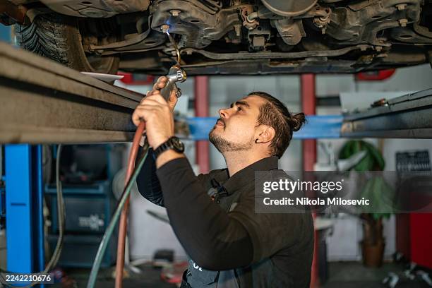 auto mechanic inspects under car while vehicle is lifted in workshop - shock absorber stock pictures, royalty-free photos & images