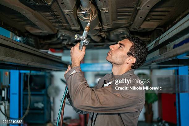 professional auto mechanic inspecting and repairing a car under lift in a busy workshop - brake pad stock pictures, royalty-free photos & images