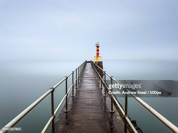 lighthouse at the end of a pier on a foggy day with calm water,amble,united kingdom,uk - information equipment stock pictures, royalty-free photos & images