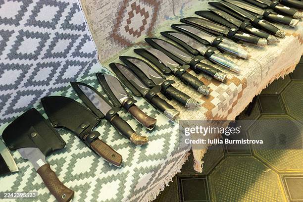 assorted fixed-blade knives lined up on patterned blankets for display and sale - switch blade stock pictures, royalty-free photos & images