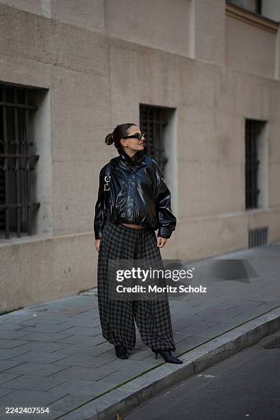 Anna Winter is seen wearing a black oversized faux leather jacket from Zara styled with voluminous checkered balloon trousers from Zara, pointed...