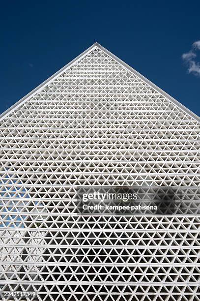 a modern triangular building facade with a repeating geometric lattice pattern of white triangles, set against a clear blue sky. - complex math stock pictures, royalty-free photos & images