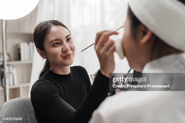 maquilleuse asiatique appliquant du fond de teint et des produits de soins de la peau sur une cliente dans un lieu de travail en studio. l’application de cosmétiques. esthéticienne professionnelle maquillage de travail - industrie de la mode photos et images de collection