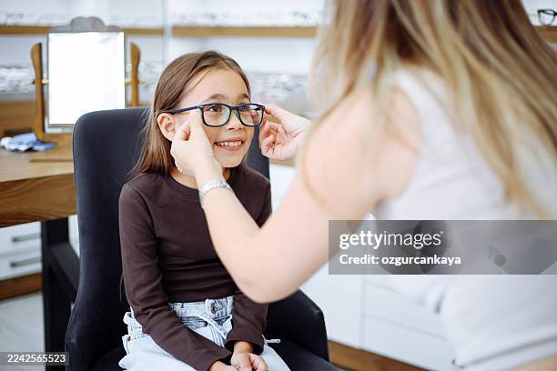 chica pequeña eligiendo nuevas gafas en la óptica - miopía fotografías e imágenes de stock