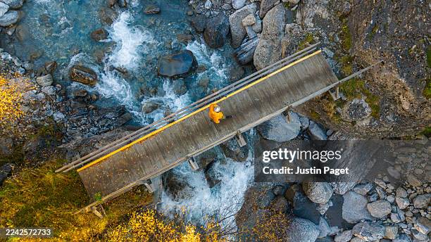 an overhead aerial/drone view of an unrecognisable person walking over a bridge that crosses a beautiful mountain stream in the french alps - french alps stock pictures, royalty-free photos & images