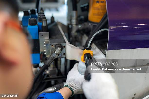 in an industrial workshop, a technician collects oil from a hydraulic system using a bottle and tube. the procedure emphasizes precision, professional maintenance, and careful handling for analysis and quality assurance. - lubrication system stock pictures, royalty-free photos & images