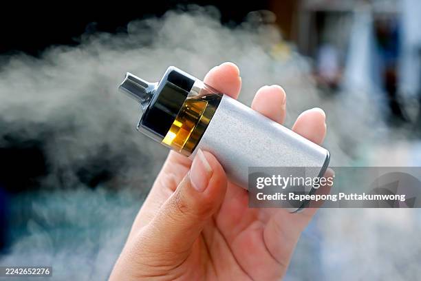 close-up of a modern vape pod system device held in a person's hand, surrounded by a cloud of white vapor, illustrating the popularity of e-cigarettes - cigarette électronique photos et images de collection