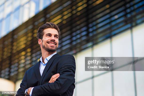 giovane uomo d'affari sorridente davanti al suo edificio ufficio - completo da uomo foto e immagini stock