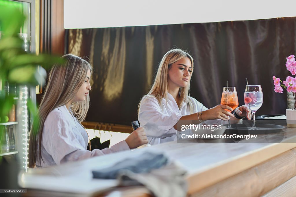 Zwei Frauen, die in einer modernen Bar Barkeeper sind und Cocktails hinter einer hölzernen Theke einschenken