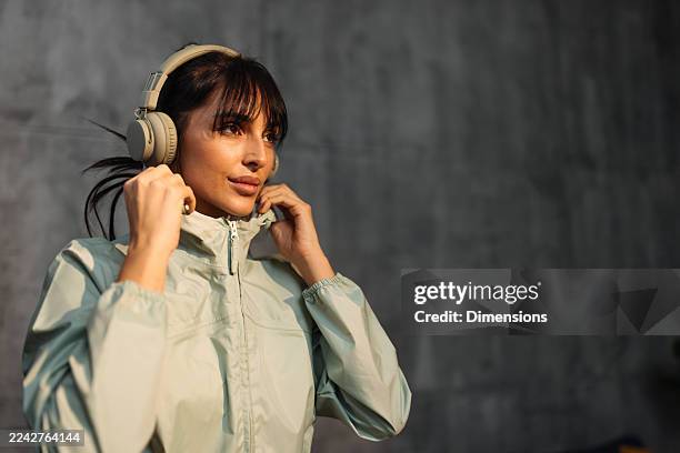 eine frau mit kopfhörern rückt ihre jacke zurecht und ist bereit für ein heimtraining in einer ruhigen studioumgebung - athleisure stock-fotos und bilder
