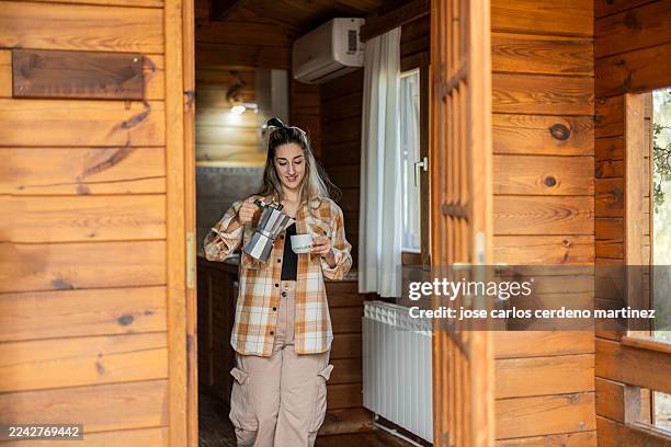 young woman pouring coffee into cup in rustic cabin - cafetera moka fotografías e imágenes de stock