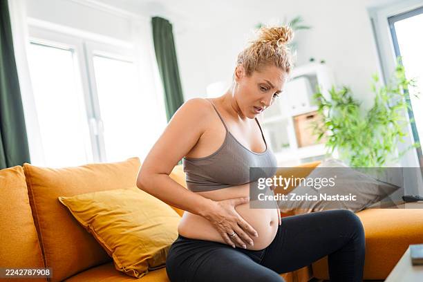pregnant woman feeling pain while sitting on sofa - menselijk hoofd stockfoto's en -beelden